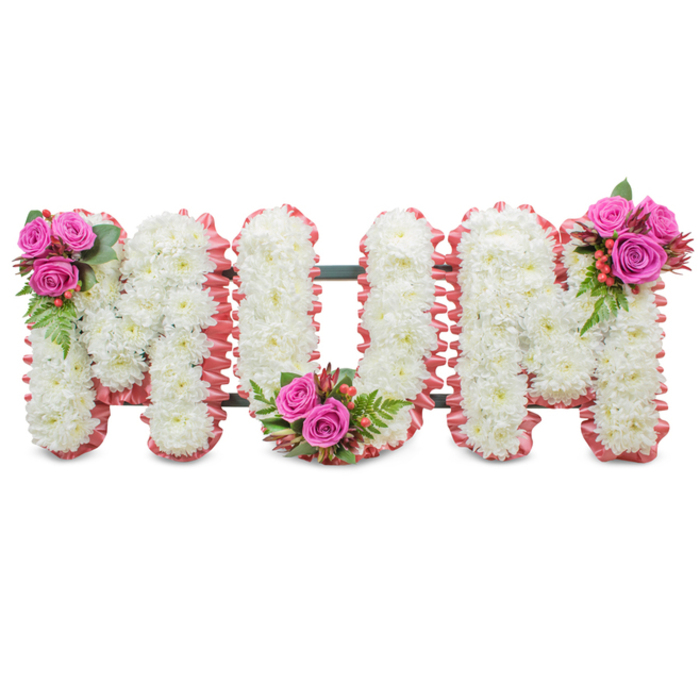 A poignant funeral tribute spelling MUM, presented against a plain white backdrop so every detail reads clearly: each letter is composed of dense, small white chrysanthemums whose layered petals form a soft, continuous mass across the face of the letters. The uniform white surface communicates purity and solemnity, while the edges of each character are finished with a lightly ruffled soft-pink ribbon that adds a subtle, comforting blush around the silhouette. Visible between the letters is a dark green structural frame that maintains the upright stance of this standing tribute without drawing focus away from the flowers themselves. Deliberate colour accents appear in three compact clusters of fuchsia-pink roses, positioned thoughtfully at the upper left of the first M, the curve of the U, and the upper right of the last M; each cluster is paired with glossy fern-like greenery and little bunches of orange-red hypericum berries that lend a livelier texture and help guide the eye across the composition. In close view the tactile contrasts are clear: the feathery, cushiony chrysanthemums, the silky petals of the roses, the smooth shine of the berries, and the gentle ruffle of ribbon-together they make a tactile, comforting statement. I can picture this piece in the gentle morning light of a service room near Bentley Priory or standing beside a family memorial at a chapel close to Stanmore station; it feels like a careful, heartfelt farewell for a mother, a design intended to soothe and honour with restrained beauty and floral finesse.