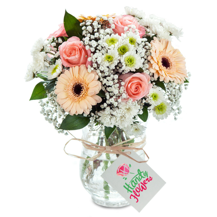 Brimming with the soft, embracing palette of Stanmore's tranquil landscapes, this meticulously arranged bouquet brings together the charm of velvety peach-pink roses-at the heart, their petals gently unfurl in romantic waves and luminous serenity. Two bold peach-orange gerbera daisies, boasting perfectly formed petals and expressive brown centers, infuse the arrangement with cheer, reminiscent of gatherings along Marsh Lane. Throughout, gentle ruffs of white baby's breath impart an ethereal lightness, bridging the main focal florals with smaller daisies of white chrysanthemum, each punctuated with an invigorating lime-green core. The interplay of crisp white and vivid green creates a sense of movement and depth, while the addition of sparse, dark green eucalyptus leaves introduces subtle fragrance and anchors the arrangement with natural texture. The bouquet is nestled in a clean, clear glass vase, its subtle surface texture catching the light and amplifying the freshness of the submerged stems. A rustic twine bow is tied precisely around the vase's neck, suspending a classic white gift tag-primed for a handwritten message of affection or celebration. Every element is professionally composed, echoing the refined yet welcoming atmosphere of Stanmore's community, and perfectly suited for all of life's treasured moments, with reliable local delivery a hallmark of local florists.
