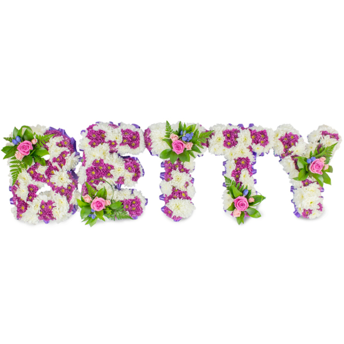 A formal, hand-assembled floral name tribute reading BETTY occupies the centre of a clean white frame, each block capital formed with careful horticultural technique. The visual weight of the letters comes from a dense base of ivory-white chrysanthemums whose compact, velvety heads are placed tightly together to produce a plush tactile surface. Contrasting magenta to deep-fuchsia chrysanthemums are used as an internal pattern and outline, accentuating the letter shapes and providing a vivid two-tone effect that makes each character immediately legible. Around the perimeters a slim band of purple fabric or ribbon is applied to create a neat edge and to echo the mid-tone purple within the letters. Three small posy-style accents punctuate the composition - on the B, above the middle bar of the first T, and on the upper arm of the Y - each posy made from soft pink roses, smaller bright-blue filler flowers (reminiscent of cornflower or delphinium), and sprigs of delicate green fern and foliage; these give vertical lift and a softer, garden-like contrast against the structured letterforms. The light is neutral and even, set to show texture rather than dramatic shadow, so the creamy whites, cool blues, warm pinks, and purples read clearly. As a seasoned florist serving Stanmore, from families meeting at St John's Church to small ceremonies near Stanmore Common, I expect this design to read as a respectful and highly personalised memorial - a name rendered in comforting materials and fine floral craftsmanship that invites touch and quiet remembrance.
