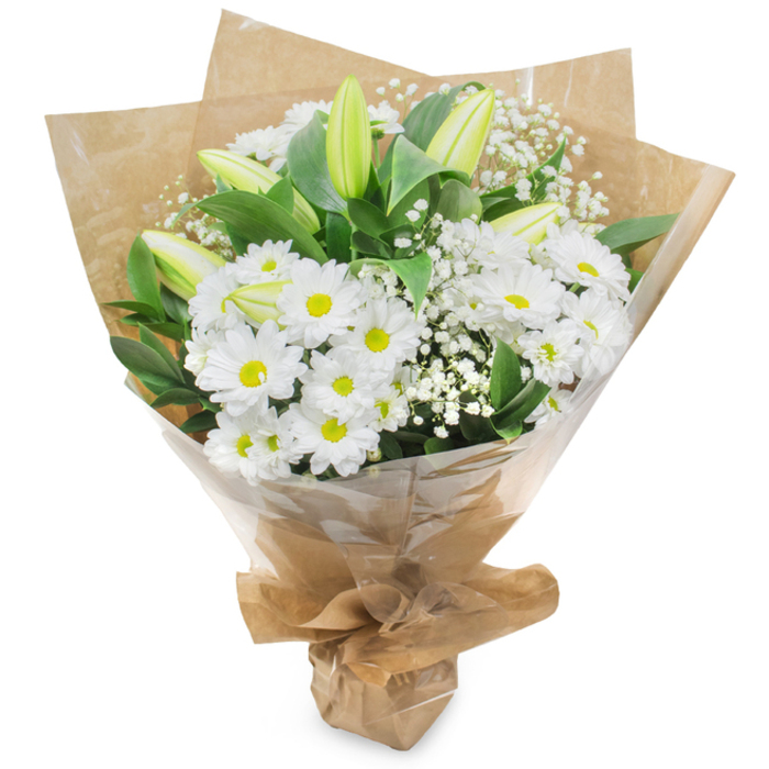 A visually restrained and luminous bouquet captured against a simple white backdrop, described with the steady voice of an experienced Stanmore-based florist. At its heart are numerous white chrysanthemum blooms, daisy-like and neatly formed, each sporting a gentle yellow center that softens the pure white petals and lends a warm focus to the composition. Rising among those rounded heads are several long, tapered lily buds in a pale green-yellow tone; their slightly striped surfaces and tight curves suggest forthcoming blossoms and a quiet sense of anticipation. Scattered throughout the bouquet are feathery sprays of gypsophila, their infinitesimal white flowers creating a translucent veil that gives depth and a light, buoyant texture. Dark green leaves and substantial stems anchor the arrangement, offering contrast and a fresh, verdant scent when held close. The bouquet is assembled by hand, wrapped first in rustic brown kraft paper that provides an earthy counterpoint to the whites, then covered in clear, glossy cellophane that preserves and presents the flowers neatly; the bottom is gathered and tied, producing a stable, portable form. The overall impression is one of composed serenity-suitable for thoughtful sympathy, gentle congratulations, or as an elegant housewarming gift. Locally, this kind of bouquet is often chosen by customers in Stanmore and nearby Harrow Weald who favour subtlety and timelessness, and it reads as both modest and refined when placed on a mantle or bedside table.