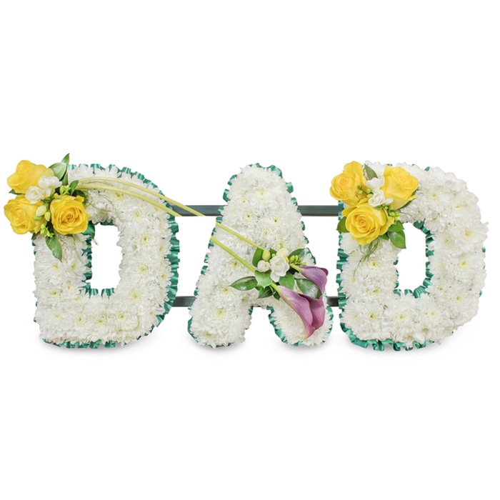 A solemn yet tender floral composition reads the single word DAD in large, freestanding letters, each letter sculpted from a thick, even blanket of pristine white spray chrysanthemums that produce a soft, cushion-like texture and a quiet visual purity. The edges of every character are carefully traced with a rich, dark green satin ribbon-ruffled slightly to add a tactile frame-so the letters sit with crisp definition against the plain white backdrop. Thin, dark green metal support rods are visible behind the arrangement, connecting the three letters into a stable, unified memorial. The left 'D' carries a glowing accent at its upper curve: a cluster of bright yellow roses, three or four in bloom, paired with tiny white filler flowers such as freesias or gypsophila and wisps of fresh green foliage; two long, slender green stems extend diagonally and upward across toward the centre, lending a gentle movement that feels almost like a reaching gesture. The central 'A' bears a contrasting cluster tucked low on its diagonal arm-two deep purple or burgundy calla lilies whose smooth, trumpet-shaped forms create a refined, contemplative focal point surrounded by small white accents. The right 'D' mirrors the left with another sunny yellow rose cluster on its upper curve, giving the whole piece balanced warmth. The scent is soft and clean-white chrysanthemums' mild powdery note, the light citrus of roses, and cool green foliage-evoking a calm morning near Stanmore Hill. This bespoke memorial is crafted to offer comfort and dignity at a funeral service or wake, an eloquent floral condolence that honours a father's life with simplicity and grace.