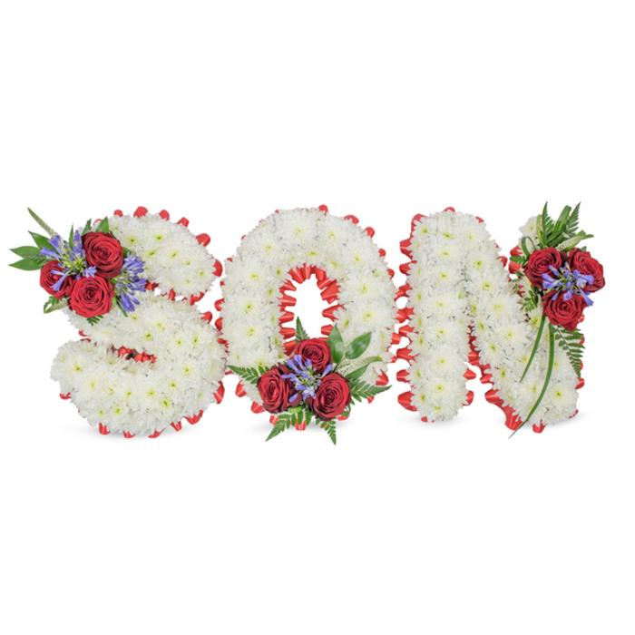 A solemn, lovingly assembled memorial arrangement spells SON in three substantial capital letters, each letter meticulously formed from dense clusters of pure white chrysanthemums that create a cloud-like, tactile surface against a simple white backdrop. The silhouette of each character is crisply traced with a bright red satin ribbon folded into a scalloped border, the vivid trim giving definition and a traditional, respectful flourish. Each letter is further punctuated by a composed spray of florals and greenery: the S is accented at its upper-left curve, the O carries a lower-centre cluster, and the N receives a placement on its upper-right stem. In these clusters, several deep crimson roses provide a velvety focal point, counterbalanced by upright blue-purple spikes-Liatris or similar-that lend a slender, architectural line, and finished with rich, dark green foliage and fern-like leaves that cascade gently. The sensory impression is quiet and layered: the soft fragrance of roses mingles with the faint, clean scent of chrysanthemums, and the contrast of textures-plush chrysanthemum heads, satiny ribbon, pointed Liatris stems-speaks to careful craftsmanship. This bespoke lettering is often chosen for chapel tributes, graveside services, or funeral receptions in the Stanmore area-perhaps delivered to a family home off Stanmore Broadway or placed at a service near Belmont Circle-offering a dignified, personal expression of love, sorrow and remembrance.