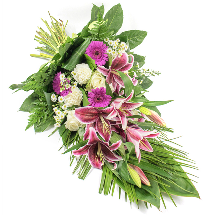 A beautifully balanced funeral sheaf is displayed against a bright white background, its elongated form gracefully angling from the upper left corner down to the lower right. This diagonal, teardrop-like shape suggests a gentle bow of the head, mirroring the sentiment of respect and remembrance it is meant to convey. At the centre of the arrangement, several striking Stargazer lilies take pride of place, their large petals saturated with rich fuchsia-pink, trimmed with luminous white edges, and delicately speckled in burgundy near the throat. Some lilies are fully unfurled, proudly revealing their star-shaped form, while others rest in partially closed buds tipped with green and blush, hinting at blossoms yet to open. Around these focal lilies, bold magenta gerbera daisies offer bright, circular accents of colour, while creamy white roses and soft white carnations lend a serene, cloud-like softness. The roses appear both in tight, elegant buds and in gently opening blooms, their layered petals signalling love and respect. Tiny white daisy-like filler flowers are interwoven throughout the composition, adding fine detail and a sense of air and light between the more substantial blooms. A lush surround of greenery frames the flowers: broad, glossy leaves provide structure and depth, delicate fern fronds soften the edges, and long, narrow blades of foliage arc and trail beyond the flowers, emphasising the piece's elongated, flowing line. Illuminated with calm, even light, each petal and leaf appears fresh and meticulously placed, as if this tribute has just been completed in a Stanmore florist's studio for same-day delivery to a local service at a church, crematorium, or cemetery. The overall effect is one of quiet elegance, compassion, and enduring remembrance.