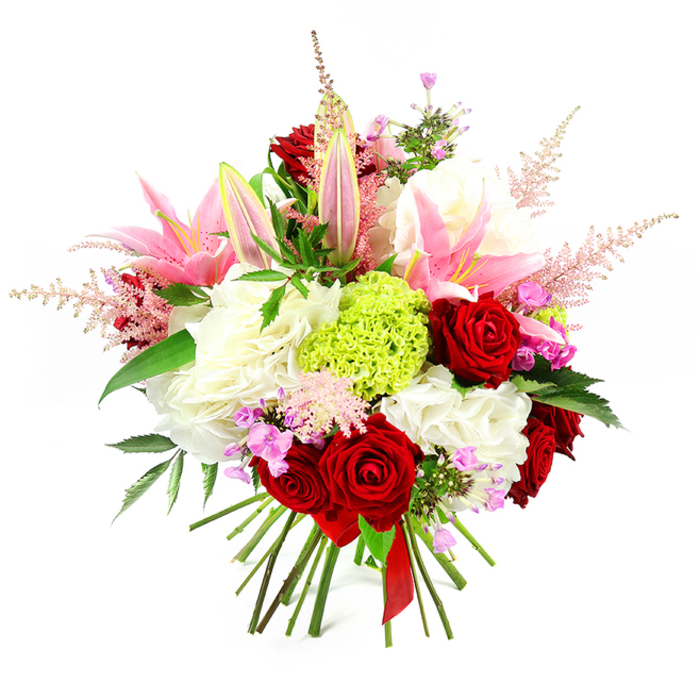 Captured against a clean white background, this richly detailed bouquet appears as a carefully composed study in romantic colour and texture, echoing the refined style favoured in many Stanmore homes. The arrangement is tightly hand-tied, giving it a rounded, dome-like silhouette, with each blossom placed to create a sense of layered depth. Deep crimson roses are scattered throughout, their velvety petals curling inward in perfect spirals that speak of classic passion and devotion. Intertwined with them are several pink lilies, some fully open with broad, satin-like petals that curve back to expose pale, delicately patterned throats and pollen-laden stamens, while others stand as smooth buds, tipped with a touch of green, symbolising blossoms not yet revealed. A generous cushion of ruffled white blooms, resembling hydrangeas or large carnations, forms the lush base of the bouquet, adding volume and visual softness, much like fluffy clouds beneath a sunset sky. In the centre, a striking lime green dianthus sphere adds a modern focal point, its fine, frilled texture catching the light and echoing the fresh greenery found in Stanmore's parks and gardens. Slender plumes of soft pink astilbe sprout from different points in the design, arching gently outward and upward, creating a feathery, romantic halo that softens the bouquet's outline. Tiny, colourful accents of fuchsia and lavender filler flowers are tucked between the larger heads, offering little sparks of whimsy and contrast. Rich, dark green foliage winds through the flowers, providing a natural frame and enhancing the vividness of the reds and pinks. At the bottom, the stems are neatly gathered and bound with a narrow deep red satin ribbon, completing an arrangement ideal for special celebrations, romantic gestures, or elegant dinner tables across Stanmore.