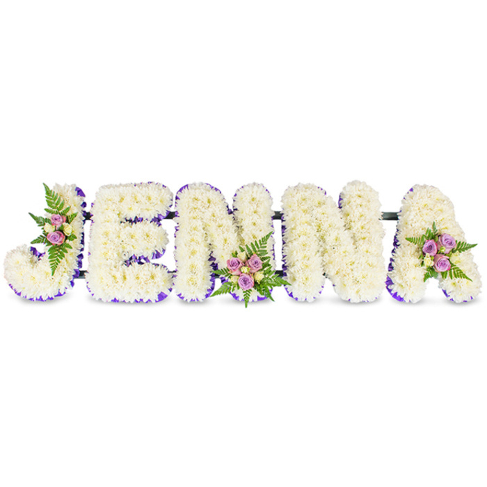 A peaceful, personalised floral name tribute spells JENNA in strong, three-dimensional capital letters set against a spotless white background. Each letter is painstakingly covered with dense clusters of small, creamy-white chrysanthemums or similarly delicate blooms, creating a soft, cloud-like texture that reads as gentle and reverent. A subtle band of violet-purple ribbon or small blossoms traces the inner edges of each letter, offering crisp definition and a quiet elegance that complements the white flowers. Three small accent posies are thoughtfully placed for balance: one tucks into the outer curve of the J, another anchors the centre of the second N, and a third nestles on the upper right of the A. Those posies blend blush-pink and lavender spray roses with a scattering of pale cream or buttery yellow roses and wisps of fresh green fern foliage, lending tenderness, scent, and a natural rhythm to the composition. Thin, dark connecting bars run behind the letters, providing a discreet structural backbone so the tribute can stand or be transported intact. The arrangement is shown in soft daylight that draws out the chrysanthemums' texture and the roses' soft hues, giving the piece an atmosphere of calm reflection. As prepared by Flowers Stanmore for local commemorations, this bespoke name tribute speaks of love, respect and remembrance - a quietly striking choice for memorial services at nearby venues such as Stanmore Broadway halls or churches around Canons Park.