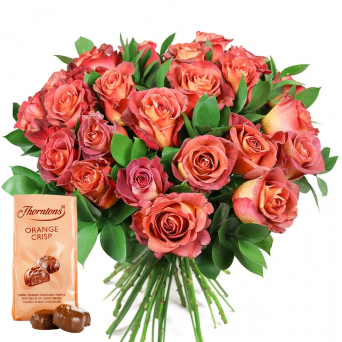 An elegantly composed image, reminiscent of Stanmore's refined charm, showcases a vibrant bouquet of fresh roses, gracefully presented on a clear white background. Center stage is a dense arrangement of blooms featuring a stunning color gradient-from creamy peach and buttery yellow centers to radiant coral, deep salmon, and warm, rosy pink at the edges, creating a dynamic bicolor effect. The velvety petals overlap closely, forming a round, luxurious bouquet that radiates abundance and attention to detail. Glossy, leafy green foliage is woven throughout, likely ruscus or eucalyptus, offering depth and vibrancy in the style favored by Stanmore's experienced florists. A neat gathering of stems is visible at the base, reflecting professional preparation. To the lower left, an elegant Thorntons Orange Crisp chocolate pouch stands upright, adorned with the classic brand name and a bold product title in dark lettering. Just below, a tempting illustration of two milk chocolate truffles teases the palate, describing the sweet combination of tangy orange truffle and crisp wafer beneath a smooth chocolate shell. Two real truffles, perfectly rounded and gleaming, rest before the pouch, inviting indulgence. This composition, alive with seasonal color and thoughtful craftsmanship, embodies an ideal present for celebrations near Stanmore: anniversaries, birthdays, romantic gestures, or simply conveying appreciation.