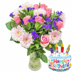 In soft morning light this birthday arrangement feels both joyful and elegantly familiar: a plentiful bouquet of fresh pink roses, pale pink Gerbera daisies and clusters of vivid purple statice, anchored by glossy dark green foliage and presented in a clear glass vase where the stems and fresh water are lightly visible. The roses range in tone from delicate blush to a richer, more saturated pink, their petals curled and layered with the reassuring softness of velvet; the gerberas reveal broad, ray-like petals and warm yellow-green centers that read like cheerful faces among the blooms. Sprays of tiny white blossoms add airiness while the purple filler lends a crisp, architectural texture that keeps the bouquet lively from every angle. Beside the vase, a cake-shaped foil balloon in white - trimmed with wavy blue 'icing', colourful sprinkles in red, yellow, blue and green, and a playful border of stars - announces Happy Birthday in multi-coloured letters. Four brightly striped candles in purple, red, orange and blue crown the balloon, each illustrated with a tiny yellow flame, and the small KALEIDOSCOPE brand mark is visible along the bottom edge. The scent is discreetly floral, a gentle rose perfume that evokes garden mornings around Bentley Priory and the quiet lanes off Stanmore High Street. A local florist touch is evident in the balanced silhouette and careful wiring of stems, and this design is a thoughtful birthday choice for same-day delivery across Stanmore and neighbouring Harrow - a gentle celebration packaged with fresh, local care from Flowers Stanmore.