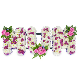Spelling out MUM in large, three-dimensional capital letters, this sympathy tribute is composed with the florist's eye for texture and balance. Each letter is a substantial block of pristine white chrysanthemums, their tiny layered petals packed to produce a plush, soft surface that suggests cloud-like comfort. Scattered through the white are concentrated patches of deep magenta or purple spray blooms that create depth and a subtle dotted pattern across the forms. Clusters of vibrant pink spray roses act as focal points: a small, neat trio at the upper left of the first M, a fuller posy of several pink roses tucked into the curve of the U, and a mirrored cluster on the upper right of the final M. Dark green foliage, notably fern fronds, fans out around each rose cluster, and a few delicate blue accent flowers are included to introduce a cool contrast.

A thin purple ribbon traces the edges while a discreet dark bar links the letters horizontally, giving the whole arrangement stability when displayed at a funeral service or memorial. The lighting in the photo is soft and neutral so the whites remain luminous without glare, and the composition reads clearly from a distance-important for viewing in chapels or near a tribute table. As experienced Stanmore florists, at Flowers Stanmore we often source fresh chrysanthemums and greens locally and craft personalised tributes for families across Stanmore, Canons Park and the nearby Bentley Priory area. This arrangement is offered as a respectful, handcrafted way to express love and remembrance for a mother, combining traditional white sympathy flowers with warm pink accents to convey both mourning and celebration of life.