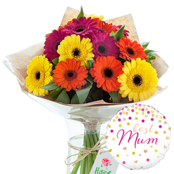 In this image, a vibrant gerbera bouquet and a tender "best Mum" balloon are styled together to create a ready-made gift that looks as though it could be carried straight through a Stanmore doorway. The central bouquet features about a dozen generously sized gerbera daisies, their broad, flat petals arranged in tidy circles around dark, velvety central disks. The colours are immediately uplifting: clear, sunny yellows, juicy oranges, and deep, jewel-like magentas with a hint of fuchsia form a lively mosaic of warm tones. Tucked among the flower heads are scattered leaves of deep green foliage, catching the light in small highlights that suggest the same freshness you might find at a florist just off Stanmore Broadway. The flowers are wrapped in a rustic layer of brown kraft paper, folded and slightly crinkled so that its edges peek above the stems, adding a natural, earthy contrast to the smooth petals. Over this sits a transparent layer of glossy cellophane that gently reflects the studio lighting, encasing the blooms while keeping the composition crisp. Around the gathered stems, a simple band of natural-coloured twine is tied neatly, its knot resting just where the bouquet meets a slim, clear glass vase. Within the vase, the freshly cut green stems stand upright in clear water, their vertical lines visible through the glass and contributing to the arrangement's tidy structure. To the lower right, a round white foil balloon brings an extra note of festivity. Its face is scattered with metallic gold and pink dots, as well as small heart shapes that drift across the surface like confetti. In the middle, the phrase "best Mum" is written in soft, flowing pink cursive, echoing the magenta tones in the flowers. Together, the bouquet and balloon evoke a feeling of warmth and gratitude, perfect for Mother's Day, a birthday celebration in Stanmore, or any occasion when a local delivery of colour and affection is the right way to say thank you.