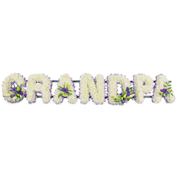 The image presents a touching floral lettering tribute where the word GRANDPA stretches horizontally across a pure white backdrop, each capital letter lavishly covered in fresh white blooms. The florist has densely packed petite white chrysanthemums or carnations across the surfaces, creating thick, rounded shapes that appear plush and full, almost like soft cushions of petals. This uninterrupted white canvas conveys purity, respect, and a serene farewell, the kind of arrangement families in Stanmore might choose to accompany a service at a local chapel or crematorium. To provide contrast and emotion, clusters of purple and lavender flowers, likely lisianthus or small chrysanthemum varieties, are artfully woven into the white letters, accompanied by sprigs of clean green foliage. These colourful highlights appear at carefully chosen points: nestled near the base of the G, in the open triangles of the As, and in the curves of the D and P. Their placement leads the eye gently from letter to letter, suggesting memories and moments gathered together. Underneath the flowers, a dark green bar runs the full length of the word, providing structural support while remaining mostly hidden, so the viewer sees only a continuous flow of blooms. This allows the tribute to be displayed as one complete piece, ideal for resting alongside other funeral flowers or as a focal point near the front of a service in Stanmore. The overall composition feels peaceful, personal, and carefully considered, as if created by a local florist who understands how much it means to see a beloved grandfather's name honoured in such a tender, graceful way.