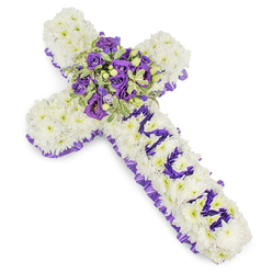 This solemn floral cross is composed with close attention to texture and messaging: a substantial foundation of small, white chrysanthemums forms a seamless, cushion-like surface that reads both pure and steady against the stark white backdrop. A ruffled, deep purple satin ribbon is woven around the entire perimeter, its satiny sheen and pleated edge lending a formal, respectful border. Down the vertical arm the letters MUM are carefully spelled by clusters of compact purple blooms-miniature lisianthus or spray chrysanthemums-each flower selected for colour consistency so the dedication reads clearly from a short distance. The central spray is a richly layered mini-bouquet of deep violet roses and lighter lavender lisianthus, their petals creating a gentle contrast of tones and a soft focal glow, complemented by variegated greens with light-edged leaves and a scattering of rounded green berries for tactile contrast. There is a subtle floral fragrance-cool and powdery-that feels consoling rather than overwhelming. This design balances simplicity and craftsmanship, appropriate for a funeral service at a local church near Stanmore tube or a memorial at Canons Park cemetery. Prepared with experienced hands and available for local delivery across Stanmore and neighbouring Harrow, this cross conveys dignity, sincere condolence, and a personal tribute to a beloved mother, executed thoughtfully by Flowers Stanmore with the neighbourhood's quiet care in mind.