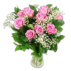 An elegant arrangement of pink roses and baby's breath is displayed in a clear glass vase against a crisp white backdrop, reminiscent of a bright Stanmore living room prepared to welcome a new baby. The bouquet features ten to twelve pink roses carefully gathered into a soft dome. Each rose offers its own character: some are still curled in tighter buds, their petals overlapping in firm spirals, while others have opened more generously, revealing plush, velvety layers that ripple outward. The colour journey runs from pale, baby-pink at the outer petals to richer, rosy tones within, creating natural depth and warmth. Between and around the roses, delicate stems of white baby's breath weave in and out, their tiny blossoms forming a light, feathery cloud that softens the structure and adds a sense of purity and innocence. Surrounding all of this, dark green leaves provide a grounding frame, their subtle sheen catching the light and emphasising the freshness of the flowers. The stems are neatly aligned within a simple cylindrical glass vase, the clear water line visible and reinforcing the impression of just-arranged blooms. The lighting is bright and even, with minimal shadow, so every detail-from the smallest Gypsophila flower to the veining on the leaves-is visible and gently highlighted. This bouquet feels quietly joyful and serene, ideal for a baby shower in Stanmore, a first visit to meet a newborn, or a thoughtful delivery to a local hospital. It speaks of tenderness, love, and celebration without overwhelming the senses, like a calm, reassuring presence at the start of a new chapter.