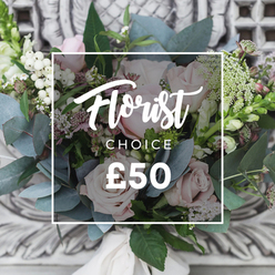 This bouquet reads like a walk through a well-loved English cutting garden: soft blush garden roses sit at the heart, their layered petals forming gentle cupped heads, while clusters of bright white berries add playful highlights like small pearls throughout the mass. Broad, round eucalyptus leaves in a muted blue-green surround and cool the palette, releasing that faint, refreshing scent that lifts the whole arrangement. Lacy sprays of tiny white blooms, likely waxflower, scatter across the composition, creating a light, drifting texture against the rose heads; small deeper pink or burgundy flowers tuck into shadowed nooks to give the bouquet depth and a touch of warmth. Vertical green-and-white flower spikes peek from the edges - suggesting snapped-open snapdragons or similar - and provide a rhythmic, elegant lift to the silhouette. The bouquet is hand-tied with a soft cream ribbon around the stems, the fabric trailing slightly and catching the soft ambient light. It rests against a subtly carved, pale stone backdrop and sits on an antique-style cream console, an image that evokes a refined, homely atmosphere. I picture this arrangement arriving in Stanmore Broadway or being chosen by someone strolling near Bentley Priory on a Sunday morning; Flowers Stanmore often designs pieces like this for milestone birthdays, understated anniversaries, or to welcome a new neighbour. Tactile and aromatic, the composition balances velvet roses and crisp greenery to create an experience of calm celebration, perfect for local delivery across Stanmore and surrounding streets.