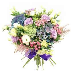 Emanating a sense of luxury and cheer, this thoughtfully arranged bouquet reflects the cultivated beauty found throughout Stanmore, from its leafy avenues to the tranquil spaces of Canons Park. At the heart, hydrangeas in deep indigo, teal, and soft purple establish a strong visual anchor, their plush, rounded forms imparting depth and calm. Soft lavender and ivory roses rest gently nearby, each layered petal evoking warmth and romance, as if hand-picked from a local rose garden at sunrise. The rich ruffles of white ranunculus are interspersed, providing supple, tactile interest that entices both sight and touch. Uplifting bursts of pale yellow eustoma and lively fuchsia-pink blooms are tastefully arranged throughout, their joyful colours reminiscent of local spring celebrations and flower shows. Ethereal pink astilbe and delicate sprays of green and white filler, suggestive of Queen Anne's Lace or Ammi Majus, add intricate detail and a breezy, fresh-picked feel. Deep green foliage weaves through the base, grounding the composition. A regal purple satin ribbon gathers the stems, imparting a final note of elegance. This bouquet offers a sensory journey-soft, fragrant, and full of romance-suitable for commemorating milestones, brightening homes, or honouring special moments for anyone in Stanmore and neighbouring communities.