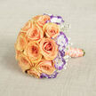 Laid horizontally on a soft, neutral linen-like backdrop and observed from a slightly raised angle, this bridal bouquet reads as a study in warm romance and refined detail. The eye is first arrested by dense clusters of peach and soft orange roses, each bloom opening in concentric spirals whose velvety petals hold tiny shifts of light and shadow. Complementing that warmth are white lisianthus with distinct violet-rimmed petals-Eustoma whose frilled edges bring a sophisticated, slightly unexpected counterpoint that enhances the roses' glow. Delicate clouds of baby's breath (Gypsophila) are woven throughout, feathering the silhouette and introducing an airy, whimsical texture that prevents the arrangement from feeling too formal. The bouquet's handle is wrapped in a light peach-salmon satin ribbon, finished at the bottom right where an elegant strand of cream pearls coils gently around the stems, offering a tactile flash of vintage glamour against the satin's smoothness. The textured beige fabric beneath-resembling linen or a fine burlap-gives the scene a handcrafted, intimate backdrop, and the soft, natural light flattens harsh contrasts so every petal and ruffle reads clearly. Imagine the scent: warm rose with faint green notes, the breath of linen and a whisper of powder from the pearls. A skilled local florist might suggest this arrangement for a Stanmore wedding near the tube station or an anniversary dinner in Harrow, where its blend of traditional and modern touches complements both church aisles and intimate garden receptions.