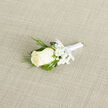 Laid at a gentle diagonal on a neutral, light beige woven cloth, this boutonniere presents a single, immaculate creamy-white rosebud as its focal point, each petal soft and meticulously formed. Clusters of tiny white gypsophila breathe around the rose like scattered confetti, lending an ethereal lightness that balances the denser greenery. Slim, feathery sprigs of deep evergreen-like foliage-reminiscent of cedar-curve outward, their darker tones accentuating the rose's pale warmth, while broader deep-green leaves form a sturdy, elegant backdrop. The stems are bound with a satin-white ribbon, wrapped with care and tied into a modest bow whose lustrous surface reflects the subdued studio light. The arrangement's textures are tactile in idea: the rose's velvet-smooth bloom, the paper-soft baby's breath, the slightly crisp, aromatic foliage and the tactile weave of the fabric beneath. A gentle, clean fragrance seems almost perceptible, the kind that lingers on a groom's lapel and recalls morning air near Stanmore Tube as wedding guests make their way from the high street to Canons Park. As a florist serving the neighbourhood, I consider proportions and wearability-this small piece pins comfortably and reads as a personal emblem of purity and hope. Flowers Stanmore prepares such boutonnieres for weddings across Stanmore and nearby Harrow, crafted to complement tailored suits and garden ceremonies with an understated, classical grace.