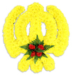 A lovingly handcrafted floral Khanda, photographed against a clean white backdrop so every detail reads clearly. The Sikh emblem - the central double-edged khanda, the encircling chakram and the two crossed kirpans - is rendered in a warm, sunlit carpet of tiny, tightly packed yellow chrysanthemum blooms that produce a soft, tactile surface and gentle three-dimensional contour. Up close you can almost feel the fine ruffled texture of the chrysanthemum petals, their golden colour catching a soft, neutral light and throwing a delicate shadow on the white surface beneath, which gives the piece quiet depth. Placed at the heart of the symbol is a compact cluster of five deep red roses; their velvety buds are arranged in a small tight rosette and nestle into a fan of dark green fern fronds that frame the red like a jewel. The contrast between the vivid yellow field and the concentrated crimson heart reads as both celebratory and solemn - yellow suggesting remembrance and optimism, red speaking of respect and enduring affection. The overall impression is of a ceremonial tribute made with exacting care: the proportions of the circular chakram and sweeping kirpans are preserved, and the floral choices emphasize texture, colour harmony and symbolic clarity. As a Stanmore florist I imagine this piece placed at a gurdwara service, a commemorative event at Canons Park, or as a dignified funeral tribute arriving for a family in the local community, its gentle scent of fresh chrysanthemums and rose underpinning the visual message of faith and reverence.