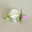 Laid carefully on a subtly woven linen cloth in a warm oatmeal shade, this boutonniere captures the essence of understated luxury and heartfelt celebration. The main flower, a pristine white Phalaenopsis orchid, opens in a broad, sweeping arc, its petals as smooth and luminous as fine satin under soft, natural light. At its centre, a gentle haze of yellow-orange and the faintest blush of pink add a whisper of colour to the otherwise snowy bloom, drawing attention to the orchid's intricate throat. Surrounding it, airy clusters of white baby's breath create a delicate mist of tiny blossoms, their cloud-like texture giving the arrangement a sense of lightness and romance. A few slim, fresh green leaves weave discreetly through the flowers, their crisp lines and glossy surfaces grounding the piece in a vivid, garden-fresh feel. To the left, three plump, pale green orchid buds rest along a slender stem, still tightly closed, symbolising new chapters yet to unfold. The stems are wrapped in a bright pink satin ribbon, finished with a neat little bow whose short tails add a playful, contemporary flourish. This buttonhole feels perfectly suited to a Stanmore wedding party heading to a ceremony near Bentley Priory or a prom night gathering at a local hotel, the kind of detail a seasoned florist would create with care for same-day delivery. The mood is one of quiet joy and polished simplicity, a single floral accent designed to sit lightly on a lapel and carry with it the promise of love, memory, and celebration.