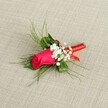 A single-stem boutonniere lies diagonally across a softly textured, light beige fabric, the kind of natural linen you might see in a Stanmore boutique near the Broadway. At its heart is a tightly furled fuchsia rosebud, deep pink petals spiralling inwards with a velvety sheen that catches the bright, even light. The rose feels full of promise, as if it is just about to open, its colour rich and saturated, evoking romance and quiet excitement before a wedding ceremony at a local Stanmore church or registry office. Encircling the central rose are dainty clusters of tiny white baby's breath, like little clouds resting against the bold bloom; their miniature, star-shaped flowers soften the composition and add a gentle, airy contrast. Around and behind the flowers, fine, feathery sprigs of bright green foliage fan outward, reminiscent of asparagus fern or light ruscus greenery, giving the boutonniere a graceful, almost ethereal frame. The foliage is interspersed with slightly broader, darker green leaves that ground the design, lending a sense of structure and balance. At the base, the stems are carefully trimmed and bound tightly with a glossy red satin ribbon, wrapped with precision so that no stems protrude, the ribbon's surface smooth and lustrous. A small, neat knot or understated bow completes the binding, adding a subtle flourish without overpowering the rose. The neutral background allows every detail of the boutonniere to stand out, from the crisp white of the gypsophila to the bright green foliage and the jewel-like pink rose, making this lapel flower feel timeless, refined, and perfectly suited to formal events, proms, or intimate celebrations across Stanmore and the surrounding North London neighbourhoods.