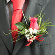 This image presents a close, almost intimate view of a wedding boutonnière, the kind often chosen by couples marrying in Stanmore's churches or local venues near Canons Park. At the heart of the design is a beautifully shaped hot pink rose, its petals layered in smooth, protective curves that seem to cup the centre like a tender embrace. The colour is vibrant without being overpowering, radiating warmth and heartfelt affection. Surrounding the rose are dainty clusters of white baby's breath, their tiny, cloud-like blossoms adding a soft contrast and evoking purity and lasting commitment. Fine, feathery blades of grass arc gently around the rose and gypsophila, providing a sense of lushness and movement that keeps the composition from feeling too rigid. Behind the main blooms, a single glossy, deep green leaf forms a subtle backdrop, its waxy surface catching a touch of light and adding structure so the boutonnière sits neatly against a dark lapel. A discreet red ribbon bow wraps the stems at the base, the knot firm but delicate, suggesting the careful attention of a florist who has prepared many such pieces for weddings around Stanmore. The boutonnière's textures invite touch-the cool, velvety rose petals, the airy sprigs of gypsophila, the smooth leaf, and the satin ribbon-while its faint fragrance brings a reminder of fresh-cut flowers delivered that morning. Ideal for a groom, best man, or special guest, it conveys a sense of personal style and quiet romance, perfectly suited to local celebrations that value beauty in the details rather than grand gestures.