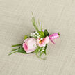 This image captures a graceful wedding boutonniere arranged with the kind of discreet elegance often chosen for Stanmore celebrations. At its centre, a single pink rose blooms in full, its layered petals forming a soft spiral of colour that deepens toward the core and fades to a gentle blush at the outer edges. The petals look silky to the touch, with just enough light grazing their surface to highlight each delicate curve. Nestled beside the rose, a few pale pink alstroemeria flowers open in elongated trumpets, their petals etched with fine lines and warmed at the base by soft yellow, drawing the eye inward. Interspersed through the arrangement, tiny clusters of gypsophila, commonly known as baby's breath, create a cloud of small white dots, adding texture and a softly romantic feel. Slim, slightly curved lengths of greenery arc gracefully around the blossoms, providing contrast and framing the rose without overwhelming it. All of the stems are carefully gathered and finished with a glossy pink ribbon, wrapped tightly and smoothly, lending a polished, formal touch that suits a groom's or best man's lapel. The boutonniere rests on a woven, neutral background that sets off the pastel colours and suggests the quiet elegance of a wedding table setting in Stanmore or a nearby venue toward Harrow. Looking at it, one can almost sense the subtle fragrance and the cool freshness of flowers prepared early in the day for same-day local delivery. The overall impression is of thoughtful craftsmanship and understated romance, ideal for marking a cherished moment.