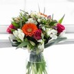 A true celebration of vibrance and fresh growth, this bouquet-composed with a Stanmore sensibility-bridges the joy of spring with heartfelt emotion. Central to the arrangement sits a bold tangerine Gerbera daisy, its vivid petals radiating cheerful warmth that invites admiration, surrounded by sculpted waves of magenta and deep crimson roses, each unfurling to reveal velvety richness. Creamy white alstroemeria arch delicately, their slender, striped petals and soft curves reminiscent of flowers blooming at the edge of Stanmore's leafy parks. White daisy-like chrysanthemums add a light, lacy texture, infusing the design with a sense of airiness. Near the top, gentle creamy or pale yellow roses soften the palette, while nested hints of lavender blossoms deepen its visual harmony. The arrangement is cradled in glossy green foliage-broad leaves encircle the base, slender spiky greens rise upward, evoking the surrounding countryside and greenways. Arranged in a classic glass vase, with stems submerged in clear, sparkling water, the bouquet is flooded by soft daylight from a nearby window, enhancing every colour and contour. Perfect for celebrating birthdays along Stanmore Hill, congratulating a dear friend, or simply brightening a quiet moment at home, this luminous bouquet reflects the thoughtful creativity and warmth of Flowers Stanmore, echoing the unique spirit of this welcoming community.