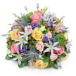 Against a pristine white background, a beautifully domed bouquet appears almost to float, its colours and textures carefully composed in a way that feels both luxurious and approachable, much like arrangements created by Flowers Stanmore for local celebrations. At the heart of the design, garden roses in soft pink, warm yellow, and delicate peach spiral outward, some petals still held close in tight buds, others fully open to reveal velvety, layered centres. Intertwined with these romantic blooms are star-shaped clematis flowers in tones of white and pale lavender, their slender petals splayed out around striking yellow centres, lending a touch of wild, cottage-garden charm. Distinctive blue eryngium-sea holly with metallic blue-grey, thistle-like heads and spiky collars-push up through the softer flowers, providing a bold, textural contrast that feels slightly untamed, like hardy plants edging the paths in Stanmore Country Park. Scattered throughout are deep purple lisianthus, some in smooth, closed buds, others just beginning to ruffle open, enriching the bouquet with cool, jewel-like depth. Bright red hypericum berries, glossy and perfectly rounded, are dotted between the petals, drawing the eye with their playful, jewel-bright sheen. All of this is held within a generous collar of greenery: broad, shiny leaves form a supportive base, while feathery sprigs and a few stems of darker, almost burgundy foliage weave up through the centre, adding subtle layers of depth and shadow. Soft, even lighting enhances every surface without harsh contrast, letting the bouquet's harmony speak for itself. It feels like the perfect arrangement for a birthday on Stanmore Hill, a thank-you gift delivered along Marsh Lane, or a thoughtful gesture for family near Canons Park, conveying warmth, care, and understated elegance.