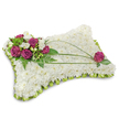 A rectangular, pillow-shaped sympathy cushion sits against a clean white backdrop, its surface densely packed with pristine white blooms-fine chrysanthemum florets (or tightly formed carnations) that read like a soft, clouded blanket under the light. The overall effect is plush and quiet, the tiny petals layered to form a soothing, tactile plane that invites a gentle touch. Around the edges a subtle border of fresh, bright green foliage and tiny green florets frames the cushion, offering a gentle contrast that brightens the composition without diminishing its solemn tone. In the upper-left corner a compact cluster of deep magenta roses, their velvety petals opening with quiet dignity, is threaded with small white accent flowers and glossy green leaves, forming a clear focal point of colour and warmth. Diagonally across the white field, from the upper right towards the centre-left, two or three slender blades of dark green bear-grass or linear foliage sweep in an elegant arc, creating movement and a thoughtful visual path that leads the eye back to the floral cluster. Near the upper-right corner a single magenta rose echoes the main spray, placed with careful balance among its own leaves to complete the composition. The soft studio lighting throws a delicate shadow beneath the cushion, emphasising the tactile depth of each bloom and the neat, handcrafted finish; the piece reads as a classic funeral tribute-calm, respectful, and composed-intended to convey peaceful rest, consolation, and lasting remembrance. This pillow-style arrangement, with its quiet palette and measured accents, is the sort of comforting floral expression families across Stanmore and nearby Canons Park often choose to honour a loved one.