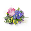 A beautifully crafted floral corsage or boutonniere rests against a clean white background, presented with the quiet confidence of a neighbourhood florist. At its centre sits an elegant rose, petals curling from a soft lavender-pink heart out to a lively fuchsia rim, the subtle velvet of each petal catching gentle, studio-like light. To the right, a compact cluster of indigo-purple florets-reminiscent of tiny hydrangea heads-offers jewel-like contrast, each small bloom marked with bright blue and lime-yellow centres that seem to glow from within. The composition is framed by varied greenery: broad, variegated ivy leaves with deep emerald cores and sunlit golden-yellow margins provide a classic, structured backdrop; softer, silvery-green foliage nods to lavender leaves and introduces a mellow, powdery texture; and delicate asparagus-fern-like sprigs weave through the arrangement, lending air and movement. A striking striped green-and-cream leaf is artfully curled to add sculptural interest, while a layer of dark purple, web-like mesh peeks from beneath the blooms, giving modern depth and subtle shimmer. At the lower right, a short strand of lustrous white pearls suggests a wristlet or a decorative fastening, adding a whisper of tradition to the contemporary palette. Imagined for weddings, proms, or milestone evenings, this corsage balances romance and modernity, the scent faintly floral, the textures inviting to touch. As a Stanmore maker I think of this worn on a lapel outside the little cafes of Stanmore High Street or pinned during a reception at a nearby community hall, a small, elegant statement that carries both personal meaning and handcrafted care.